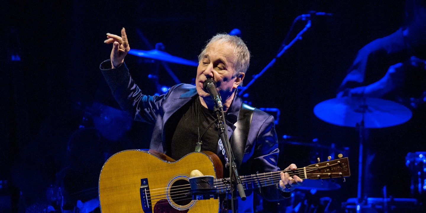 picture of Paul Simon playing guitar at a concert